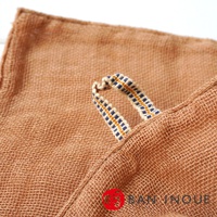 特寫鏡頭顯示了三層蚊帳棉織廚房拭巾的一角，織物為淺棕色，紋理清晰。一條帶有藍色和黃色格子圖案的懸掛環巧妙地縫合在織物邊緣。