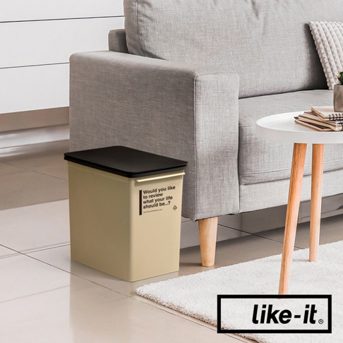 米色掀蓋式矮版垃圾桶，配有黑色頂蓋，側面印有英文文字標籤。