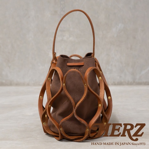 日本HERZ職人手作皮革Organ編織水桶包 G-98，咖啡色帆布內袋搭配手工編織的駝色皮革外網，復古設計，頂部提把，側邊有品牌標誌。