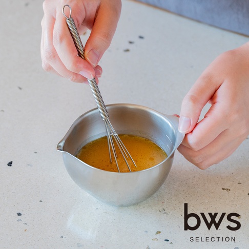 一位使用者正在使用金屬打蛋器攪拌 bws SELECTION 不鏽鋼料理備料盆中的蛋液，該備料盆設計小巧且邊緣設有導流嘴，畫面呈現俯視視角，展示不鏽鋼材質在烹飪備料過程中的實用性。
