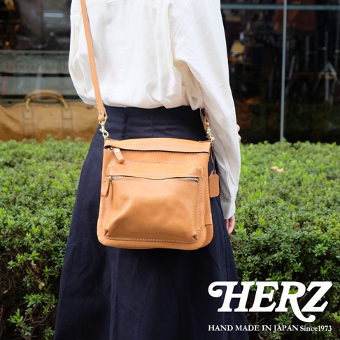職人手作皮革翻轉雙色直式斜背包，採用淺棕色皮革製作，包身有兩層拉鍊口袋，搭配同色系縫線和金屬拉鍊。