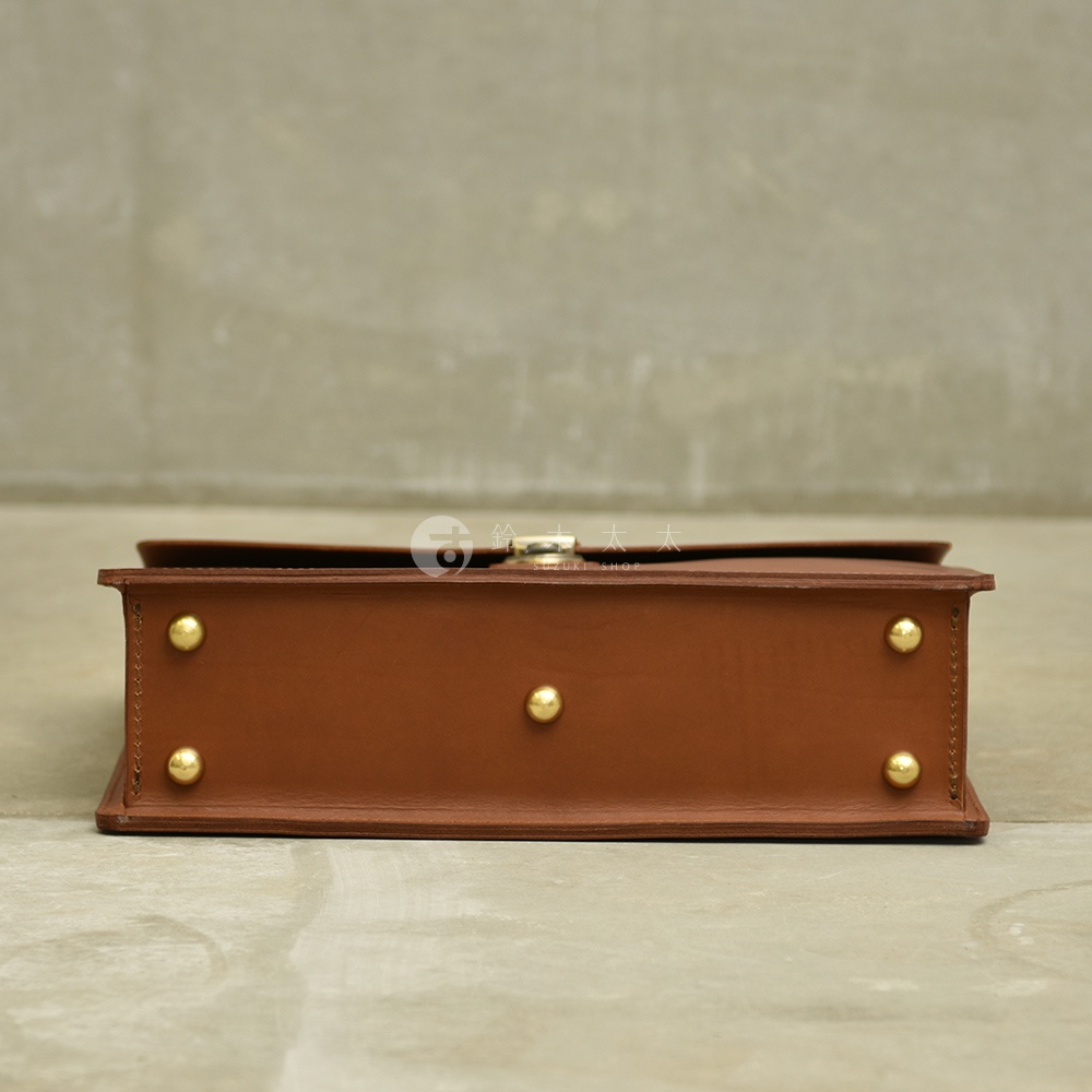 職人手作皮革Organ兩用商務公事包 G-93，側邊視角，呈現經典棕色皮革材質，包身側面有三個金色圓形铆釘裝飾，頂部配有金色金屬旋轉鎖扣。