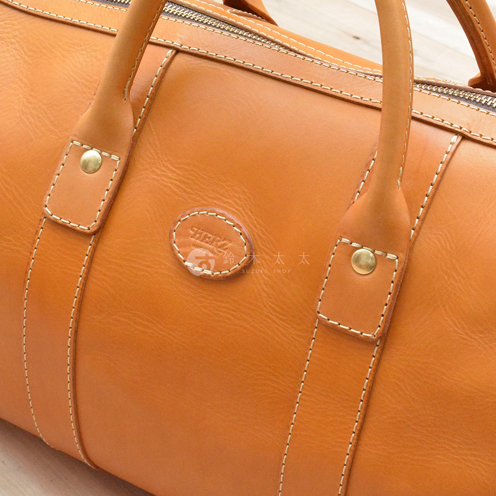 棕褐色皮革職人手作波士頓包，拉鍊開合，附有圓形皮革標誌和雙提把。