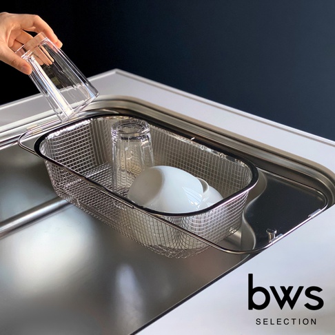 不鏽鋼網格瀝水籃，籃內有兩個玻璃杯和一個白色馬克杯，一隻手正將一個透明玻璃杯放入籃中。