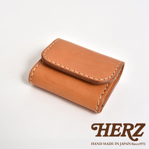 日本職人手作皮革零錢包，選用質感細膩的淺棕色皮革，採雙折式設計搭配車縫線細節，簡約精緻的質感呈現，右下角印有品牌 HERZ HAND MADE IN JAPAN Since 1973 標誌。