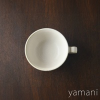 一個白色美濃燒湯杯碗，帶有米白色的六魯粉引釉，邊緣略帶淺褐色，碗身內壁有旋紋，右側有一個方形把手，置於深棕色木質背景上。