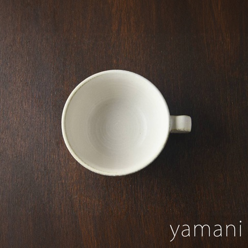 一個白色美濃燒湯杯碗，帶有米白色的六魯粉引釉，邊緣略帶淺褐色，碗身內壁有旋紋，右側有一個方形把手，置於深棕色木質背景上。