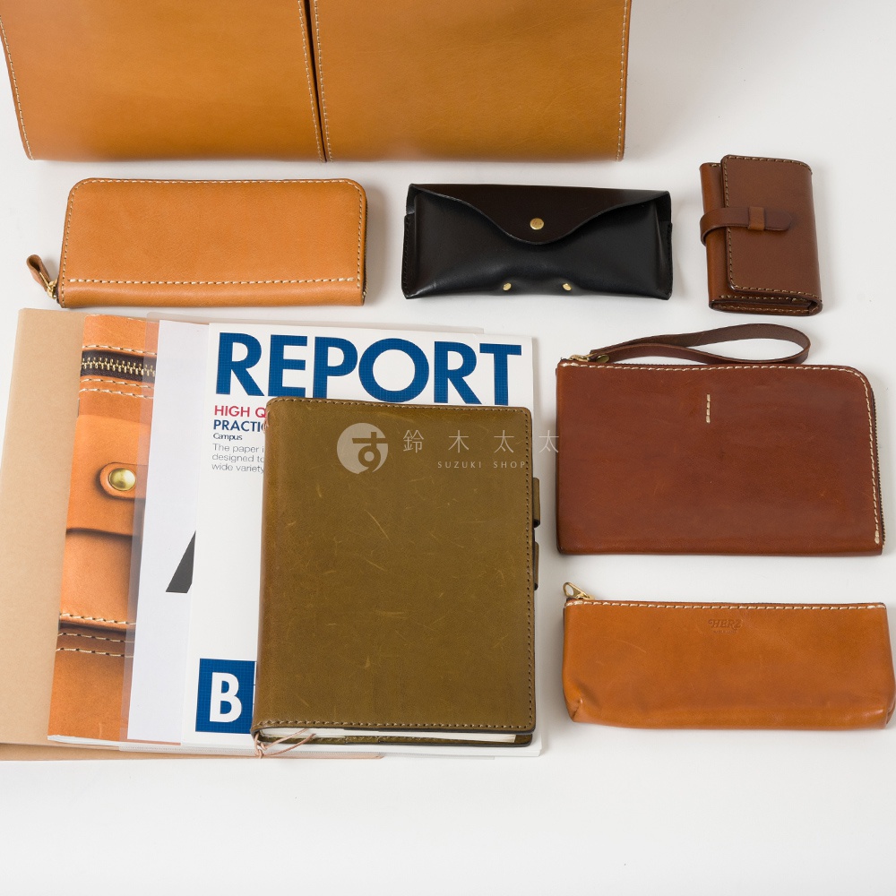 多款皮革製品，包含焦糖色、深棕色、黑色與橄欖綠的長夾、筆記本、零錢包及卡夾，材質為皮革。