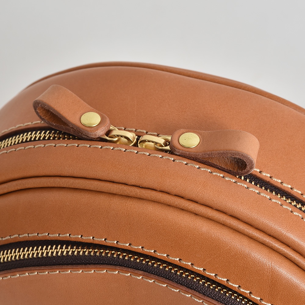 職人手作皮革小圓包，採用光滑的棕褐色皮革，搭配黃銅拉鍊及同色系皮革拉頭，車縫線細緻。