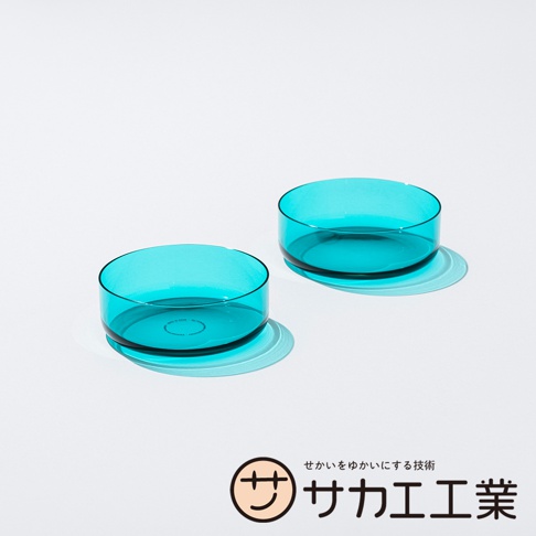 SAKAE 標誌旁為日文文字「せかいをゆかにする技術 サカエ工業」，圖片左側和右側各有一個藍綠色透明圓形碗，碗呈淺盤狀，底部有陰影，背景為純白色。