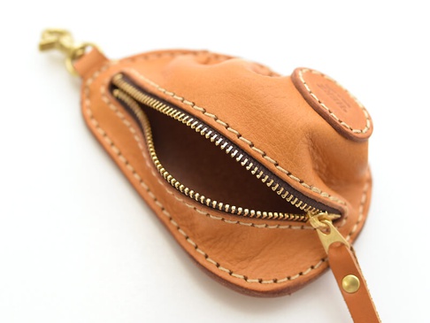 一個由棕色皮革製成的餃子造型零錢包，配有金色拉鍊和黃銅掛鉤，手工縫製，細節精緻。