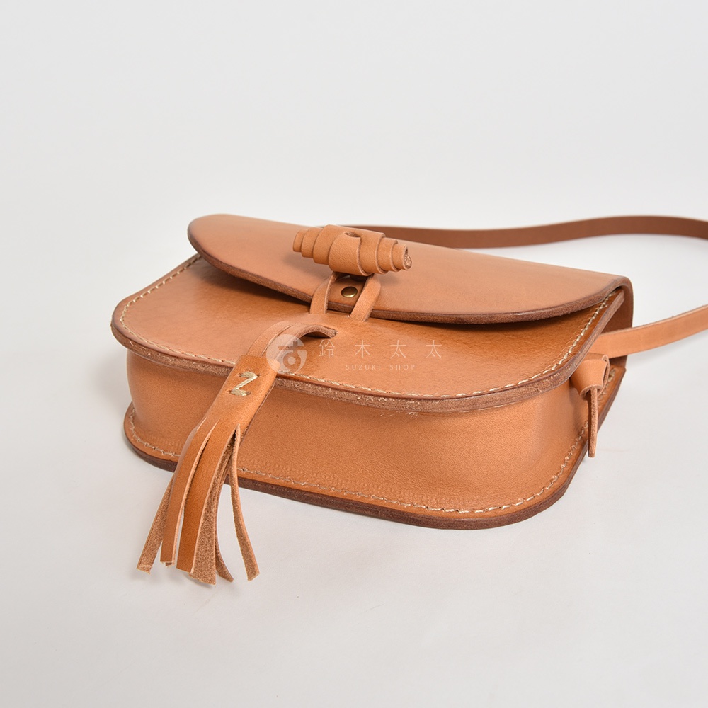 職人手作皮革流蘇側背包，淺棕色，全皮革材質，帶有捲軸式鎖扣及皮革流蘇裝飾，簡約設計。