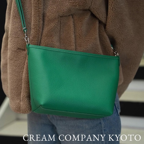 皮革隨身側背包，鮮豔綠色，觸感紋理清晰，配有銀色金屬釦環與細長肩帶，簡約方形設計，縫線精緻。