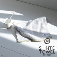 YUKINE 雪中漫步有機棉蓬厚毛巾，淺灰色，質感蓬鬆柔軟，帶有品牌標籤，旁邊有一個白色馬克杯，杯中有牙刷。