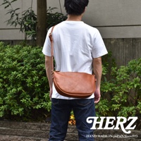 日本HERZ職人手作皮革半圓馬鞍包，棕色皮革，從背面拍攝，包包斜挎在身，搭配牛仔褲。