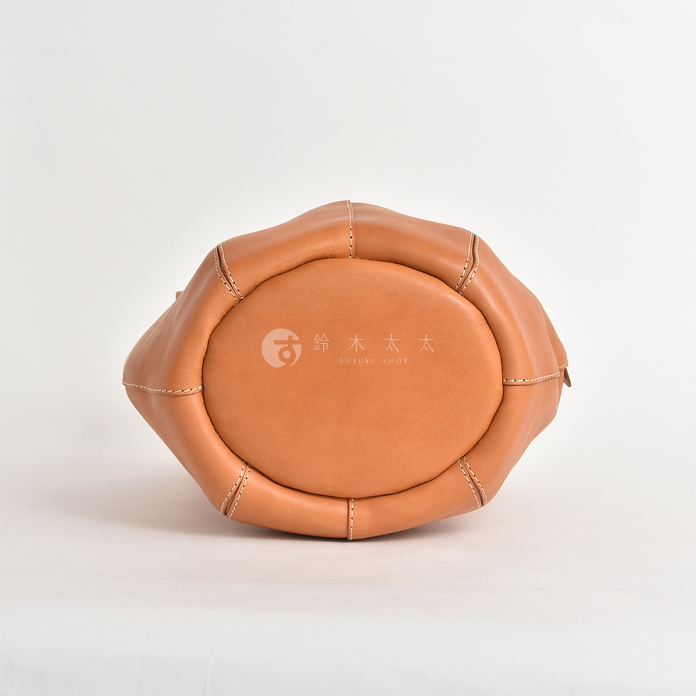 職人手作皮革球形肩掛托特包，展示皮革的自然紋理與精緻縫線，包體呈飽滿的圓潤狀，顏色為溫暖的淺棕色，底部印有品牌標誌。