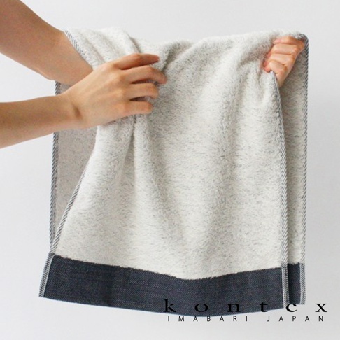 一條淺灰色、帶有細緻織紋的長纖有機棉斜紋浴巾，底部滾邊為深藍色斜紋布料，邊緣有細條紋裝飾。