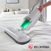 銀色雙氣旋偵測除蹣清淨機，配有透明綠色集塵筒，手柄為銀白色，放置於白色床鋪上。