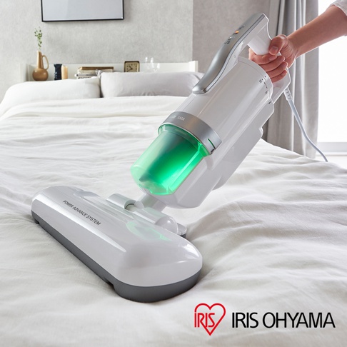 銀色雙氣旋偵測除蹣清淨機，配有透明綠色集塵筒，手柄為銀白色，放置於白色床鋪上。