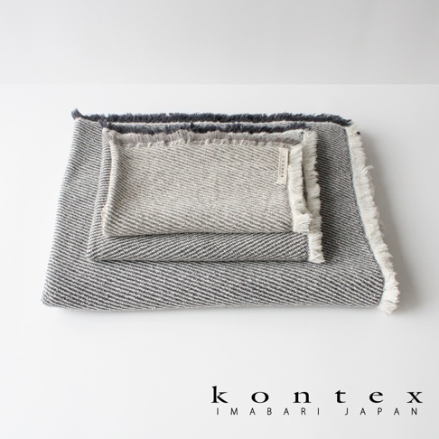 三條堆疊的浴巾，表面有斜紋編織紋理，邊緣有流蘇設計。兩條為灰色與淺灰色交織，一條為淺灰色。