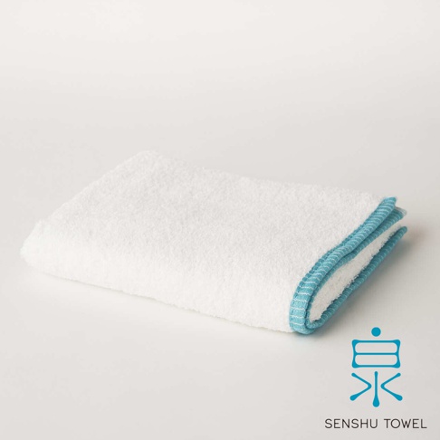 白色長纖迷你浴巾，邊緣有藍色滾邊，材質觸感細柔蓬鬆。