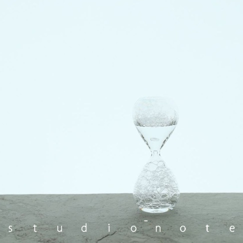 透明玻璃製成的泡泡計時器，裝有清澈的水和細小的氣泡，呈現沙漏造型，置於灰色紋理的表面上，背景為淺藍色調。