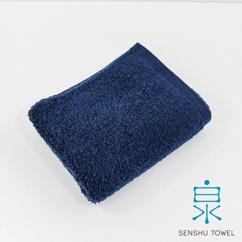 深藍色長纖毛巾，質地蓬鬆柔軟，邊緣有縫製的滾邊。