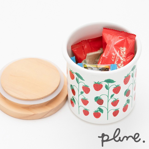 白色琺瑯儲物罐，飾有紅色草莓圖案，配以天然木紋木蓋，罐內裝有紅色包裝的零食。
