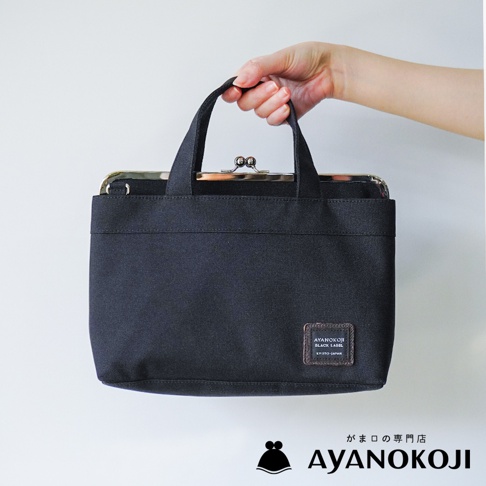 KYOTO JAPAN 品牌黑色口金手提包，由手握住提把，包上飾有品牌標籤。