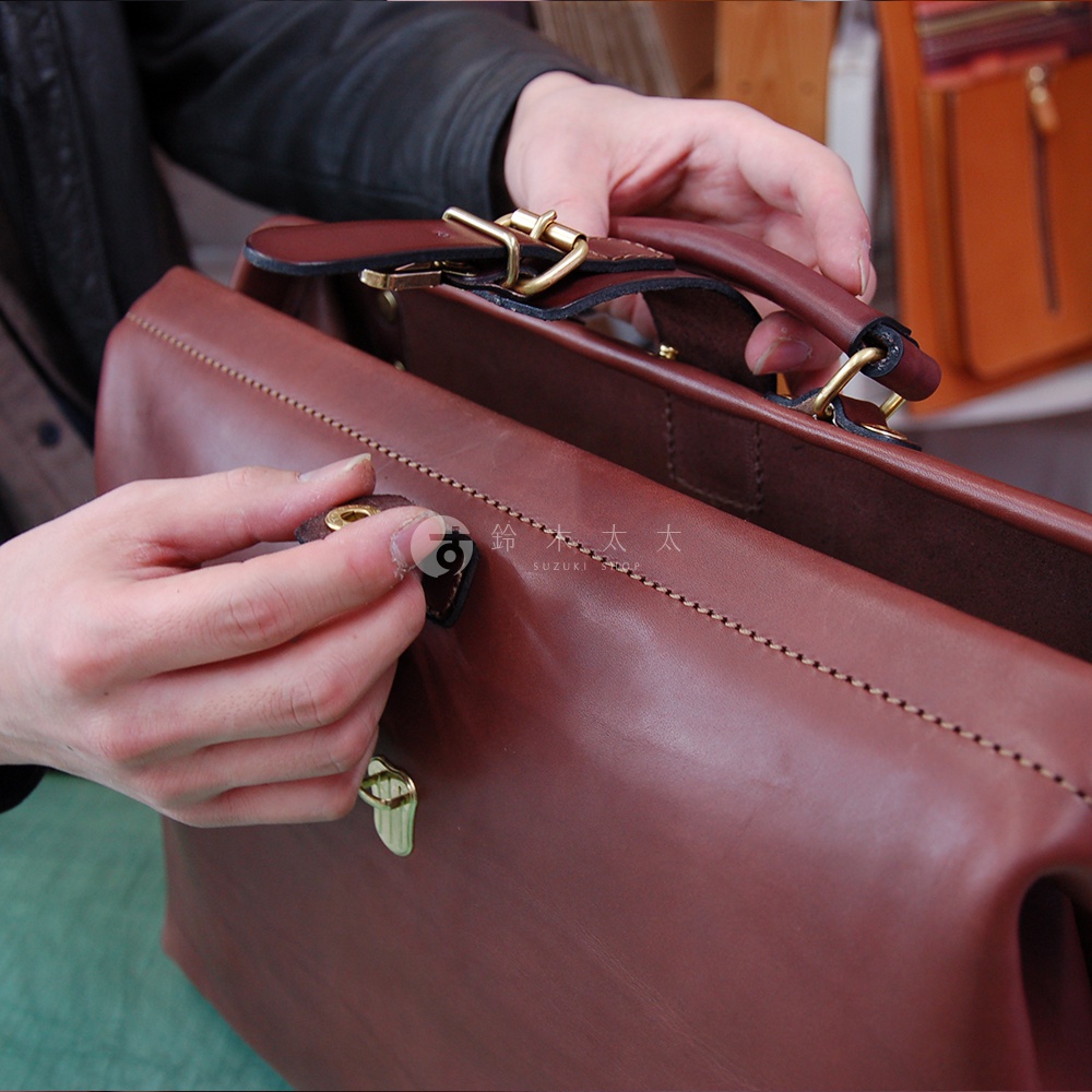 職人手作皮革軟式杜勒斯包，深棕色皮革，配有黃銅色金屬扣環和提把，包身縫線精緻。