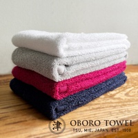 一疊四條不同顏色的毛巾，由上至下分別為白色、淺灰色、桃紅色和深藍色。毛巾材質看起來柔軟蓬鬆，並堆疊在木質表面上。