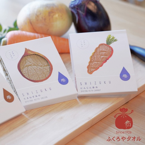 SHIZUKU野菜染瞬吸薄毛巾，包裝盒上印有洋蔥和胡蘿蔔圖案，展示了產品的天然染色特色。毛巾材質柔軟，有三種顏色可選。