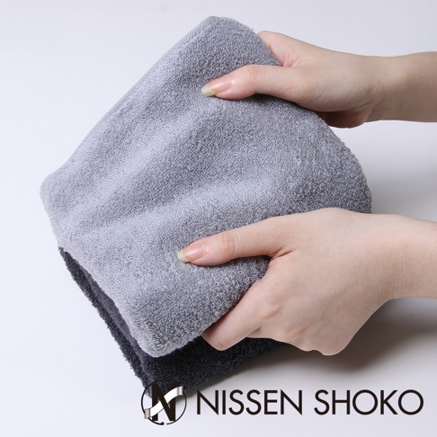 兩隻手正在展示一條淺灰色的長毛巾，其材質柔軟，毛圈細緻。下方疊著一條深灰色的同款毛巾。