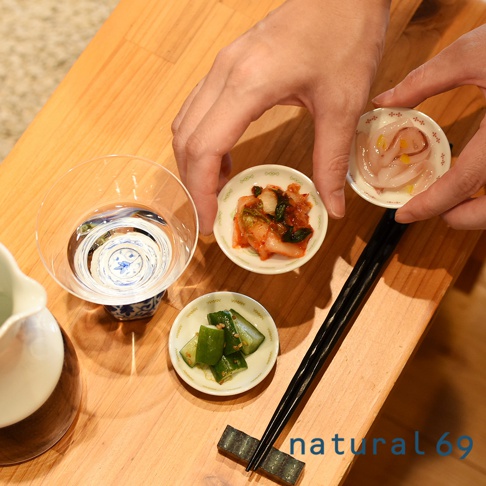 手繪風迷你小菜碟，盤中盛有泡菜、醃黃瓜及其他醃漬小菜，搭配日式清酒杯與木質餐桌。