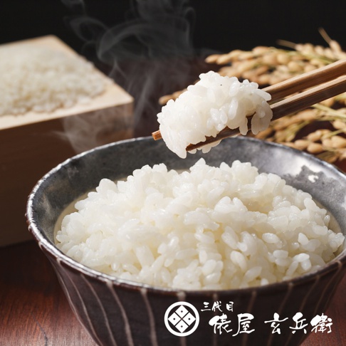 一碗熱氣騰騰的北海道七星米，米粒飽滿潔白，呈現誘人的光澤。一雙木筷正夾起一撮米飯，準備送入口中。背景是木製米箱和稻穗，營造出質樸自然的氛圍。