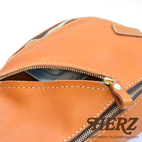 職人手作皮革多功能收納斜背包，展示皮革的自然紋理與縫線細節，拉鍊部分可見內部收納空間，呈現溫潤的焦糖棕色調。