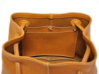 職人手作皮革兩用托特包，採用棕褐色牛皮製作，包身車縫白色線條。內部有兩個開放式隔層和一個小口袋，袋口處有綁繩設計。