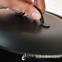 手握黑色深型鍛鐵炸鍋的鍋蓋把手，鍋身呈現深黑色，材質為鍛鐵。