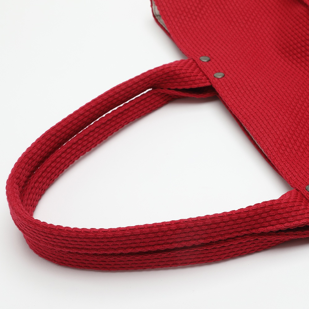 紅色的三河木綿刺子織大開口托特包，特寫其雙層提把和包身紋理，以及固定提把的鉚釘。