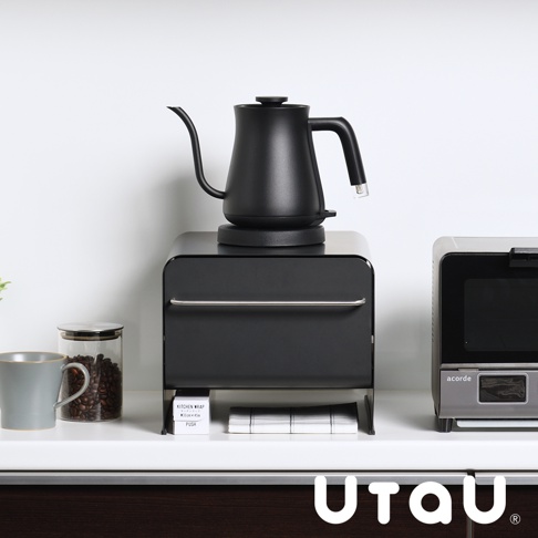 黑色抽屜式多功能萬用收納整理櫃，上方擺放黑色細長嘴咖啡壺，櫃子前方有銀色拉柄。左側有灰色馬克杯和裝有咖啡豆的玻璃罐，右側有小型銀色烤箱。