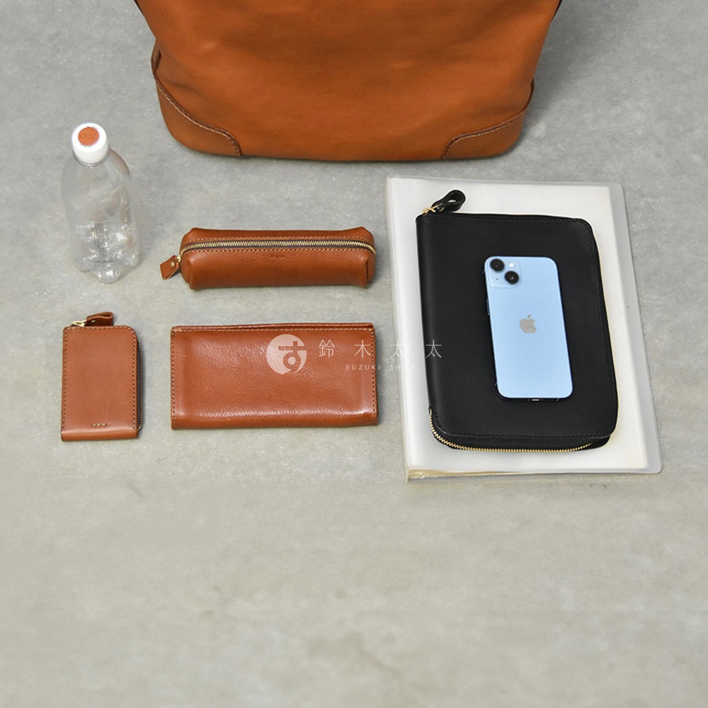 上方為職人手作皮革Organ肩背拉鍊托特包，展示其內容物，包含一個皮夾、一個筆袋、一個零錢包、一個手機及一瓶水。