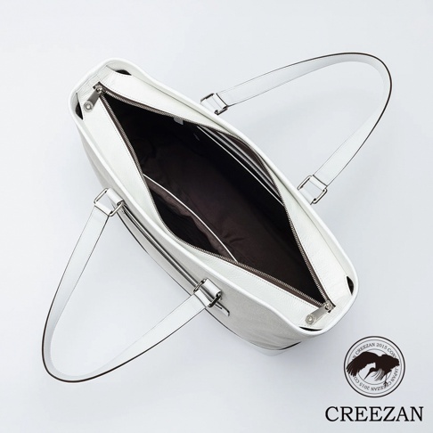 這是一款從上方俯瞰視角的 CREEZAN 品牌大托特包，包身採用白色皮革與帆布拼接材質，配有銀色金屬拉鍊與兩條白色皮革肩帶，內部設有深色織物襯裡與分層隔間，整體呈現簡約精緻的質感，右下角印有該品牌的紙鶴標誌與 CREEZAN 字樣。