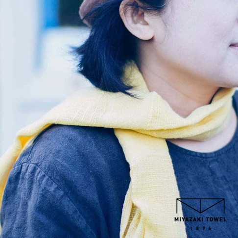 今治匹馬棉經典圍巾，淺黃色，材質柔軟，觸感細緻，圍繞在深藍色上衣上，展現簡約風格。