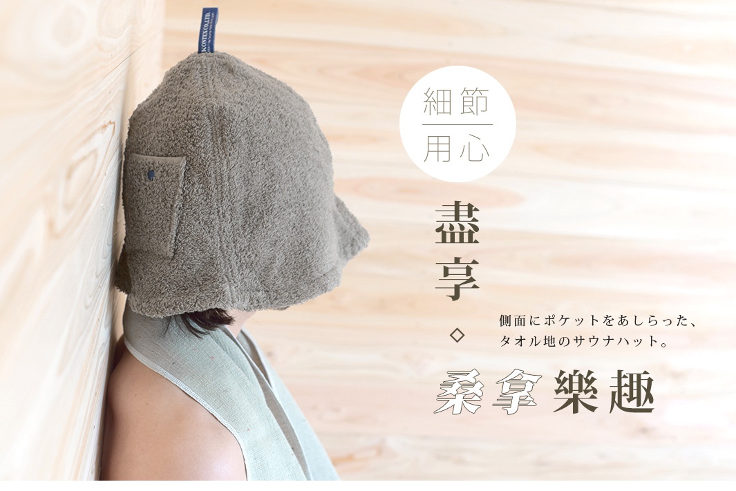 灰色毛巾材質的桑拿帽，側面有口袋，帽子頂部有品牌標籤，背景為淺色木紋。