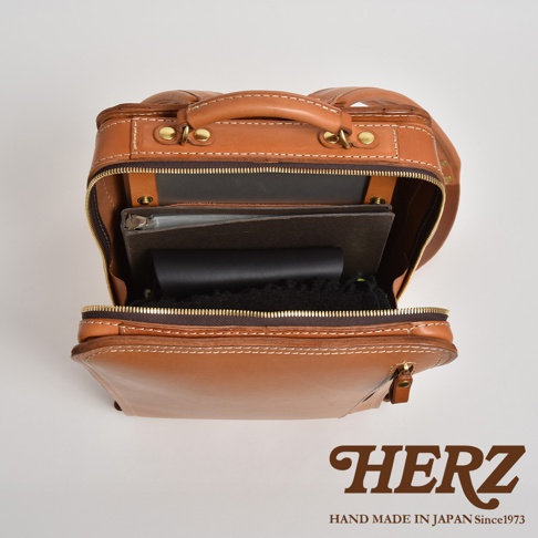 職人手作皮革商務電腦後背包 R-25，採用棕色皮革製作，包款主體開口處可見內部收納空間，其中擺放有筆記本、文件夾及黑色物品。