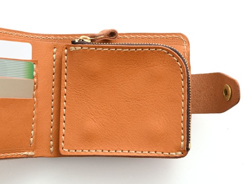 職人手作皮革短夾，採用天然皮革材質，呈現溫潤的淺棕色調。內部設有多個卡槽，並有拉鍊零錢袋設計，邊緣以白色縫線裝飾，質感細緻。