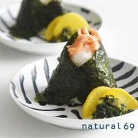 白色陶瓷盤上盛著兩個被海苔包裹的飯糰，飯糰內餡為鮭魚鬆。盤子邊緣飾有黑色手繪線條。旁邊擺放著黃色醃漬物和綠色小菜。