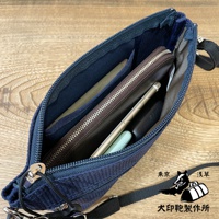 深藍色刺子織斜背包，拉鍊敞開，露出內部收納空間，可見錢包、手機、薄型手機殼等物品。