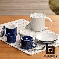 藍色M型壺，搭配同色系杯子、小奶盅，以及白色茶壺、盤子和湯匙，置於條紋布上。