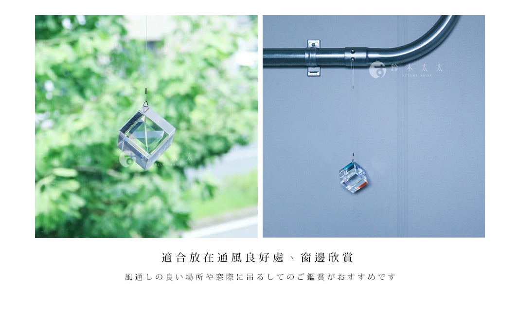 透明水晶立方體吊飾，內部有菱形切面，透過光線折射出彩虹色澤，懸掛於細線之上，背景為模糊的綠葉或淺藍色牆面。